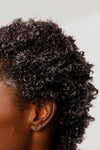 Close-up of a person with textured hair on a plain background displaying the beneifts of the Grace Eleyae Leave In Conditioner